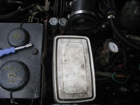 1985 Ford Bronco - A close-up view of an engine bay shows the radiator coolant and washer fluid caps, a blue-handled tool, and a white plastic container. A pr…