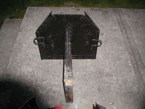 1985 Ford Bronco - A black metal object with a handle is resting on a concrete surface. The object appears to be a cooking grate or a small grill.