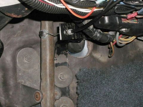 1985 Ford Bronco - A close-up view of the driver's side footwell area of a vehicle, showing a cable mechanism attached to a metal bracket near the steering co…