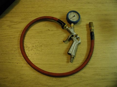 1985 Ford Bronco - A tire inflator gun with a pressure gauge and a red hose is laid out on a wooden surface.