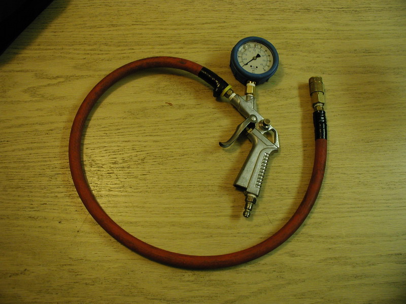 Tire inflator gun with pressure gauge and red hose on a wooden surface.