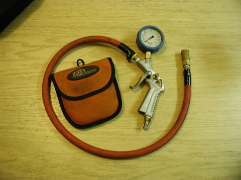 1985 Ford Bronco - A tire inflator with a pressure gauge and a small orange storage pouch are laid out on a wooden surface.
