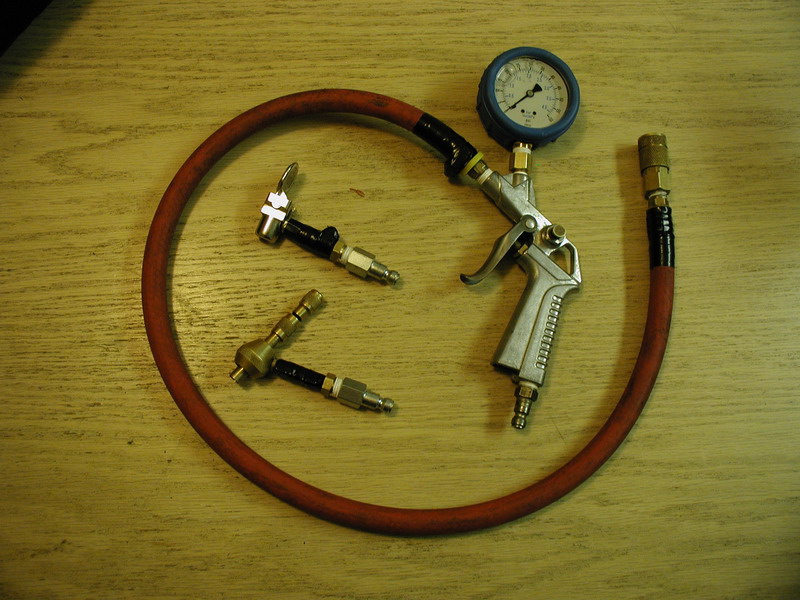 Air pressure gauge, blow gun, and tire chucks on a wooden surface.