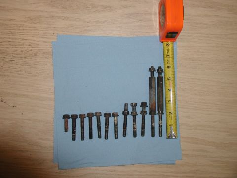 1985 Ford Bronco - A collection of various bolts and studs are laid out on a blue cloth next to an orange measuring tape. The bolts vary in size and some show…