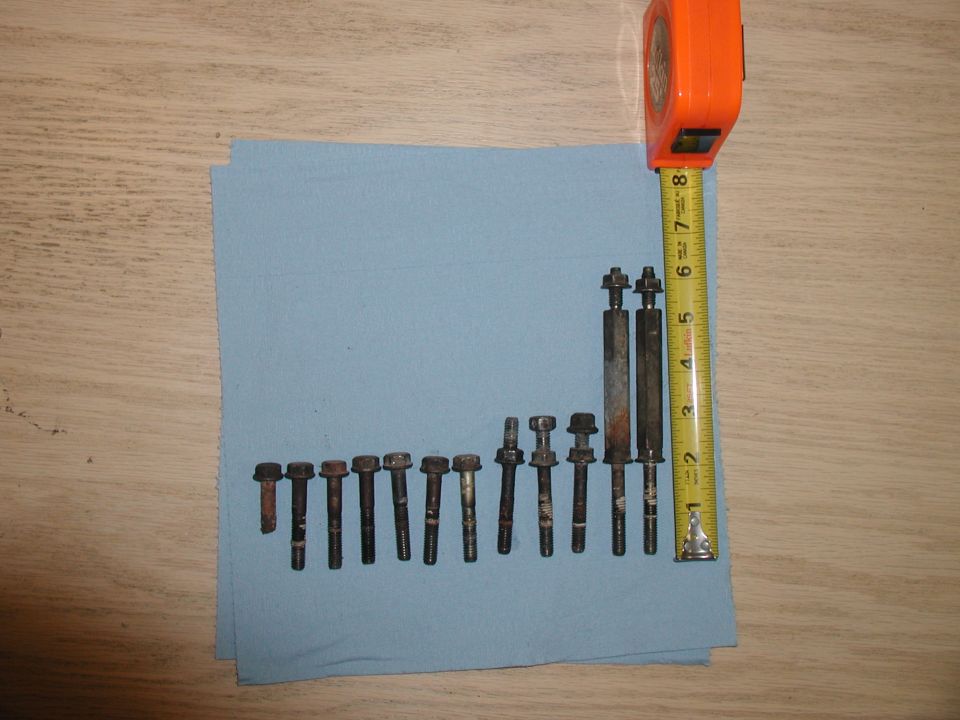 Various bolts and studs on a blue cloth next to a measuring tape