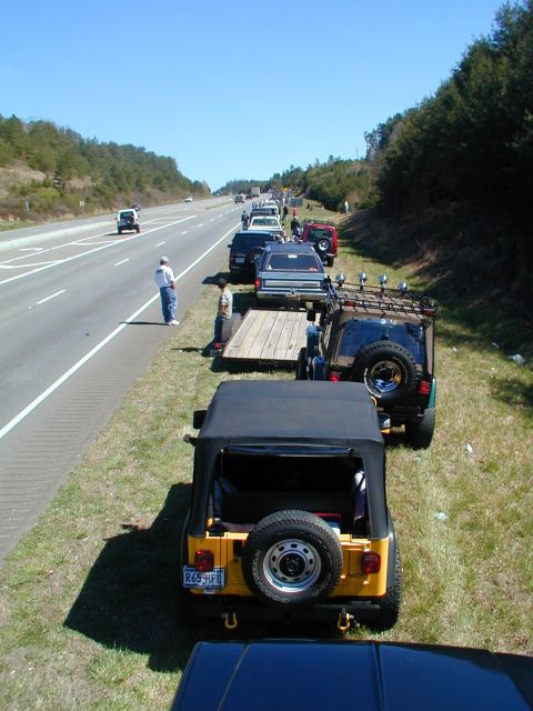 1988 Ford Bronco - A convoy of Jeeps is pulled over on the shoulder of a highway on a sunny day.