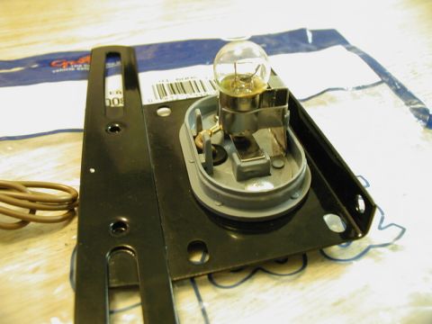 1985 Ford Bronco - A close-up view of a vehicle's taillight assembly, featuring a clear bulb, gray plastic socket, and a black metal bracket with mounting hol…