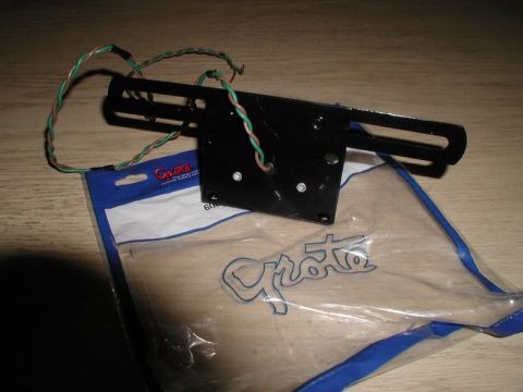 1985 Ford Bronco - A black metal license plate bracket with attached wires rests on top of a clear plastic bag with blue trim and the word "Grote" printed on…