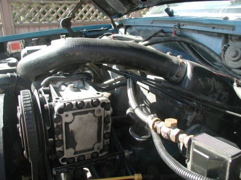 1985 Ford Bronco - Close-up view of the engine bay of a blue Ford Bronco, focusing on the air conditioning compressor and associated hoses and lines. The engi…