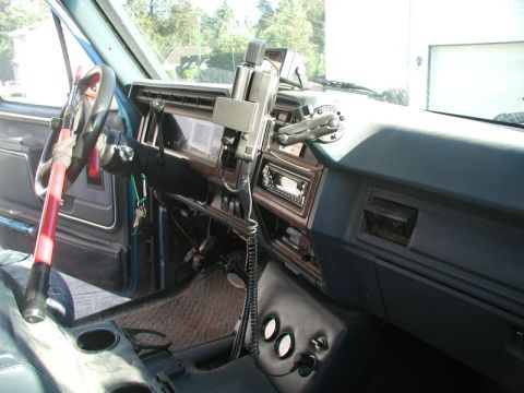 1985 Ford Bronco - Interior view of a blue Ford Bronco, showing the dashboard, steering wheel with a red and white steering wheel lock, and center console.