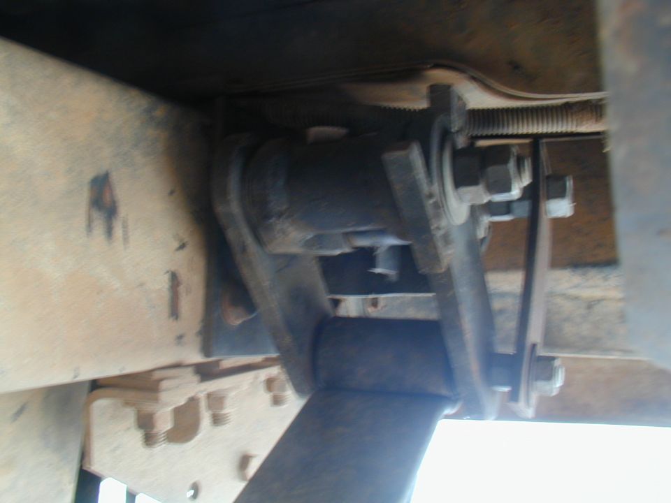 Close-up of a vehicle's suspension component, likely a shackle or bracket, with bolts and metal framing visible