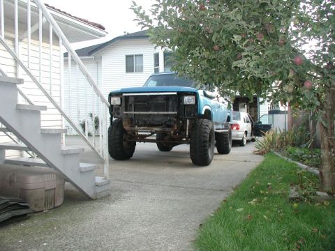 1985 Ford Bronco - A lifted, light blue Ford Bronco with large off-road tires is parked in a driveway next to a white house and an apple tree. The front grill…