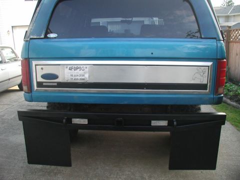 1985 Ford Bronco - The rear view of a teal Ford Bronco shows a license plate reading "4F0P9G" and a black aftermarket bumper with large mud flaps. A cartoon s…