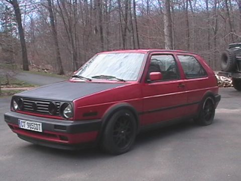 1996 Ford Bronco - A red Volkswagen Golf GTI sits parked on a driveway, its matte black hood contrasting with the body.