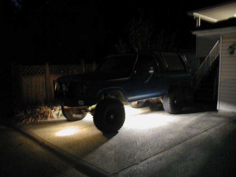 1985 Ford Bronco with large tires parked at night, headlights on.