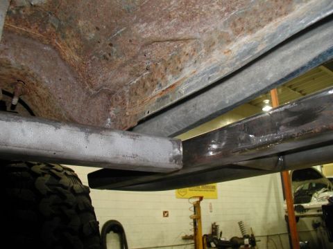 1985 Ford Bronco - The underside of a vehicle shows significant rust on the frame and body panels. New metal tubing has been welded to reinforce the frame.