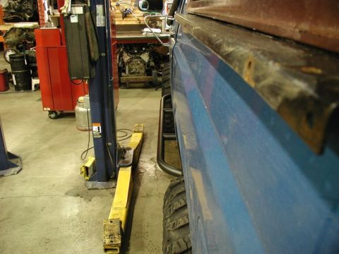 1985 Ford Bronco - A close-up, side profile view of the lower body and tire of a blue vehicle, possibly a truck or SUV, in a garage setting. A yellow car lift…