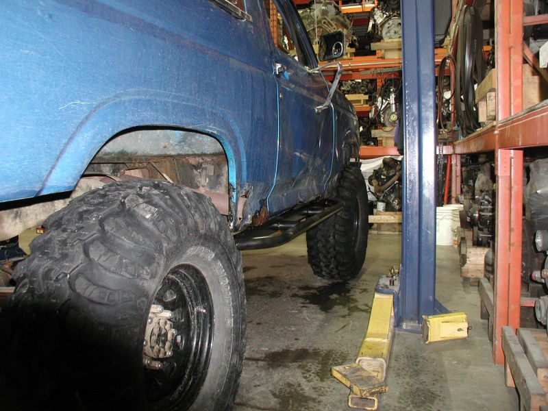 Blue Ford Bronco on a lift with large tires, showing rust on the body.