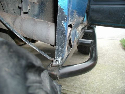 1985 Ford Bronco - A close-up view of the rusted rocker panel and custom black metal rock sliders on a blue vehicle, with a large tire in the foreground.