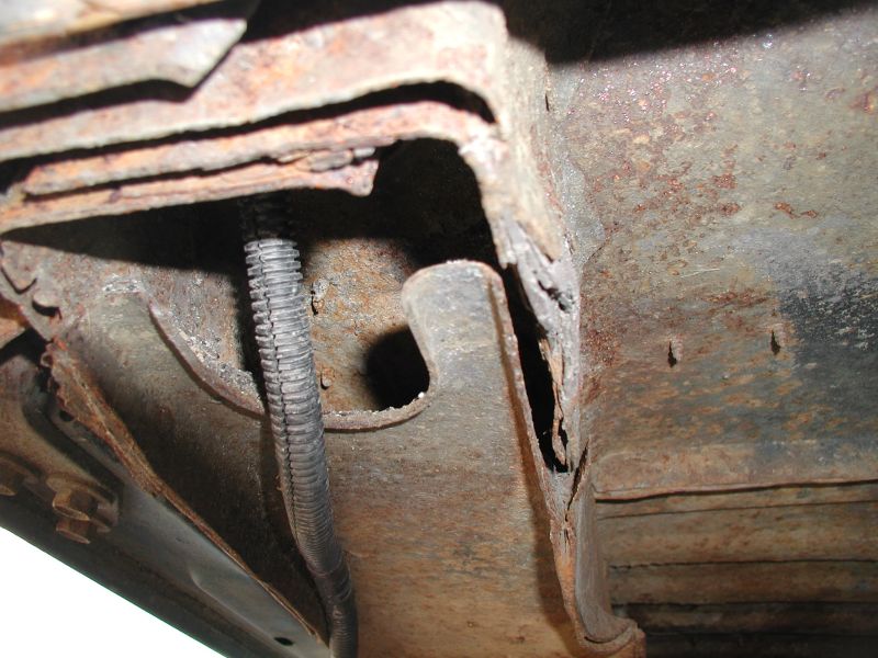 Underside of vehicle frame with heavy rust and a black conduit.