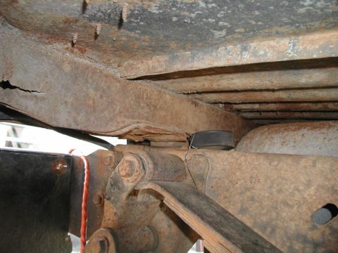 1985 Ford Bronco - The underside of a heavily rusted vehicle frame shows significant corrosion and damage, with visible leaf springs and suspension components.