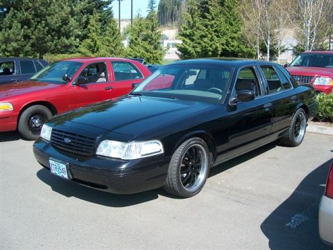 2001 Ford Crown Victoria - A black 2001 Ford Crown Victoria is parked in a lot with other vehicles.