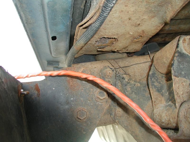Close-up of rusty vehicle undercarriage with orange wire.