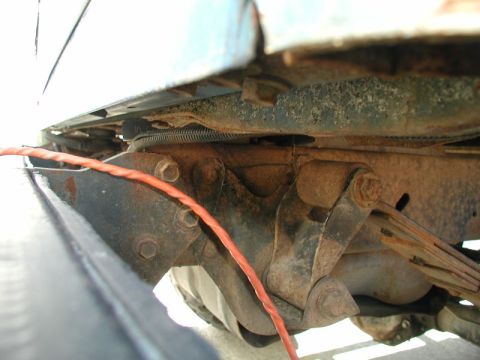 1985 Ford Bronco - A close-up view shows the underside of a vehicle's frame, focusing on the rusty leaf spring suspension system and a bright orange wire runn…