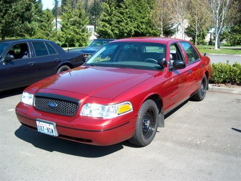 2001 Ford Crown Victoria - A red 2001 Ford Crown Victoria is parked outdoors, showing its front 3/4 view with black steel wheels and a visible license plate.