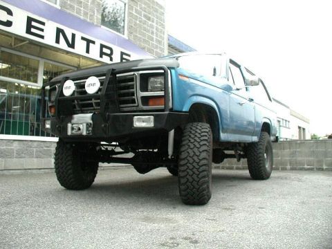 1985 Ford Bronco - Ground-level 3/4 front shot of a lifted blue Ford Bronco showing the black steel front bumper with winch, tube brush guard and two covered…