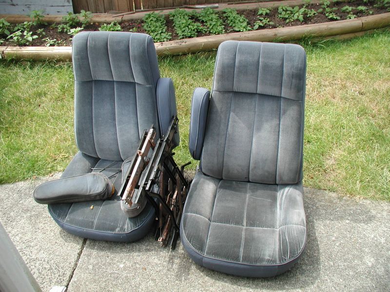 Two dark gray velour car seats with armrests on a concrete patio.
