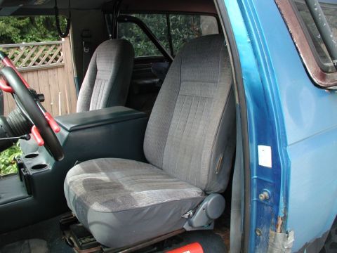 1985 Ford Bronco - The interior of a blue Ford Bronco shows the driver's seat, center console with cup holders, and part of the steering wheel. The driver's s…