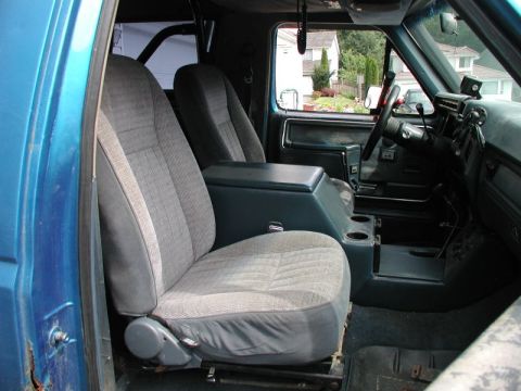 1985 Ford Bronco - The interior of a blue Ford Bronco shows the driver's side bucket seat, center console with cup holders, and dashboard with steering wheel.…