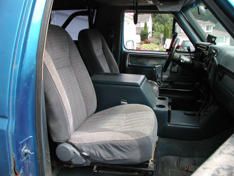 Interior of a blue Ford Bronco showing front seats, center console, dashboard, and roll cage.
