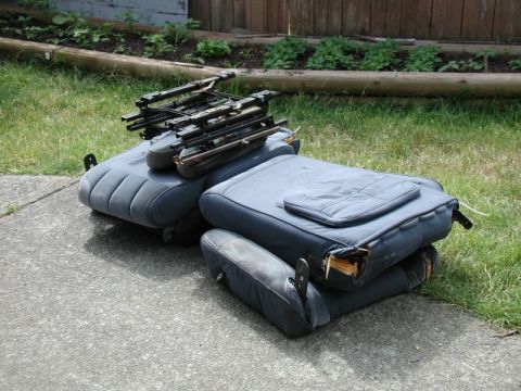 1985 Ford Bronco - Two dark blue car seats are stacked on top of each other outdoors on a concrete driveway next to a grassy area. The top seat has a metal fr…