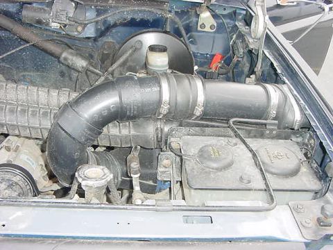 1985 Ford Bronco - Close-up of the front of a Ford engine bay showing a thick black molded snorkel intake tube clamped in a long S-bend across the radiator su…