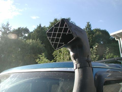 1985 Ford Bronco - Close-up of a black Safari-style snorkel head with a diamond-mesh grille, clamped to the ram tube and rising above the A-pillar of a blue S…