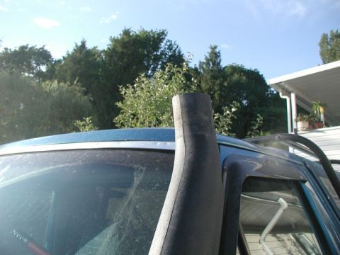1985 Ford Bronco - Black snorkel ram tube mounted along the passenger A-pillar of a blue SUV with the intake head removed, showing the open tube end above the…