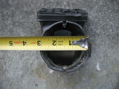 1985 Ford Bronco - Black snorkel intake tube lying grille-up on concrete with a yellow Lufkin tape measure hooked on the rim, reading roughly 3.5 inches acros…
