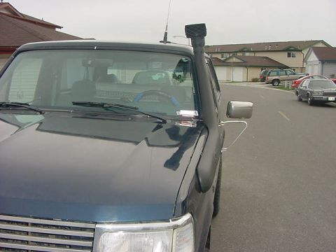 1985 Ford Bronco - The front passenger side of a dark colored SUV is shown parked on a residential street. A snorkel intake is visible mounted on the A-pillar.