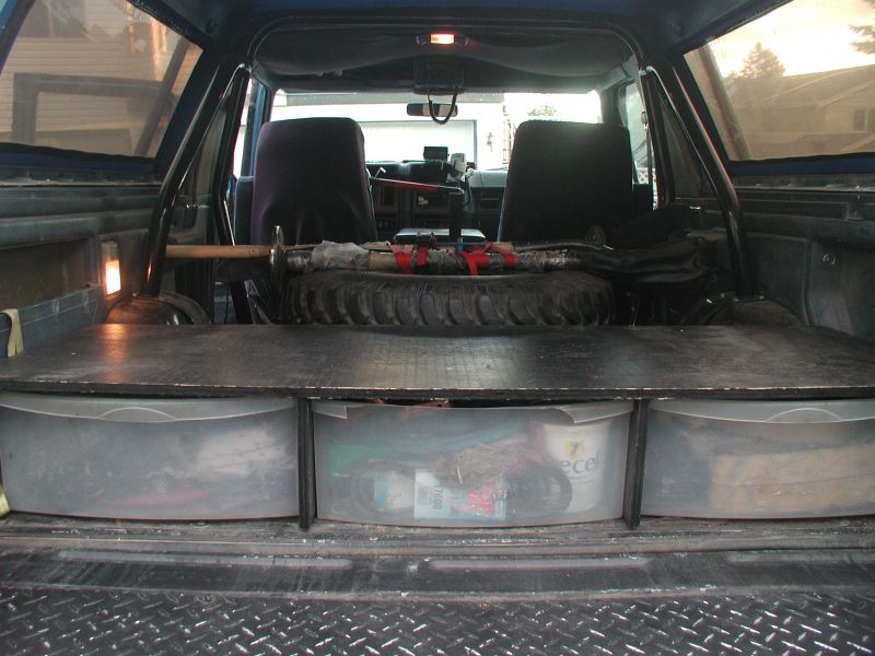 Interior rear of a blue Ford Bronco with custom storage bins and a spare tire.