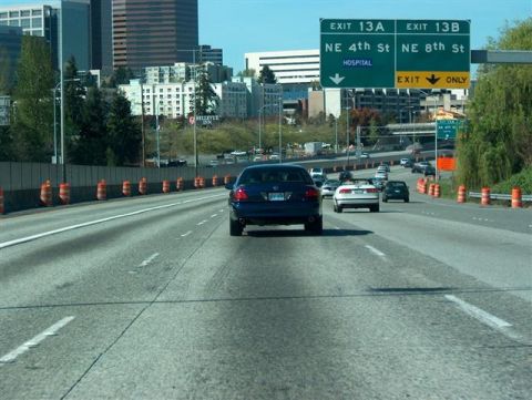 2001 Ford Crown Victoria - A blue sedan drives on a highway with city buildings in the background and overhead exit signs.