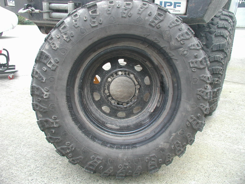 Close-up of a Super Swamper off-road tire on a black rim.