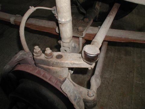 1985 Ford Bronco - A close-up view of the suspension and braking system of a vehicle, showing the brake rotor, shock absorber, leaf springs, and tie rod ends.
