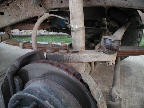 1985 Ford Bronco - Close-up view of the front suspension and brake assembly of a vintage Ford Bronco, showing rusted leaf springs, a shock absorber, and a bra…
