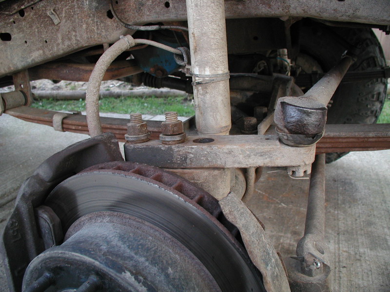 Close-up of rusted Ford Bronco front suspension, leaf springs, shock, brake rotor and caliper.