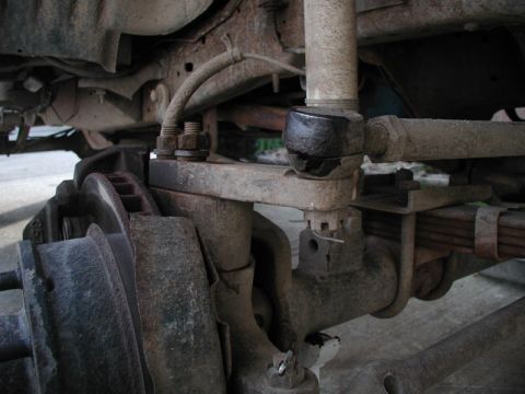 1985 Ford Bronco - A close-up view of the rusty front suspension and steering components of a vintage vehicle, likely a Ford Bronco, showing the tie rod end c…