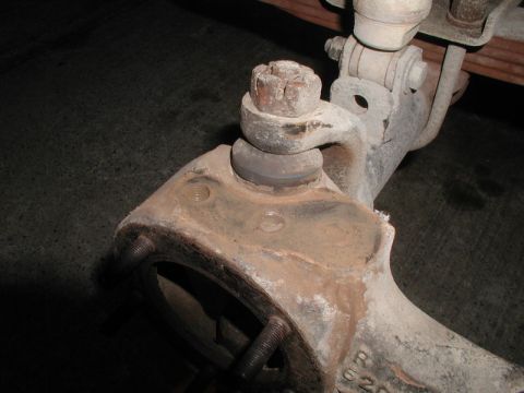 1985 Ford Bronco - A close-up view of a rusty suspension component, likely a ball joint assembly, on a vehicle. The part is heavily weathered and shows signs…