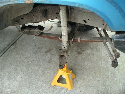 1985 Ford Bronco - The underside of a blue vehicle, likely a truck or SUV, is shown supported by a yellow jack stand. Visible components include leaf springs,…