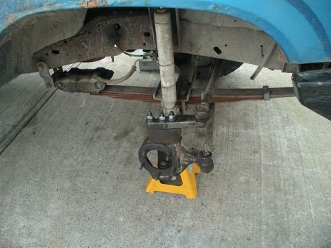 1985 Ford Bronco - The underside of a blue Ford Bronco's front suspension system is shown, with the wheel assembly removed and supported by a yellow jack stan…